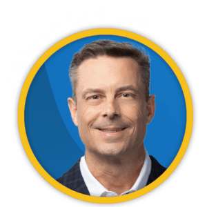 Portrait of a smiling middle-aged white man with grey hair, wearing a suit, framed in a yellow and blue circular border.